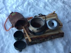 an assortment of cooking utensils are laid out in the snow on a piece of wood