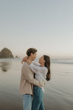 a man and woman are standing on the beach with their arms around each other as they hug