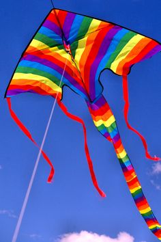 a rainbow colored kite flying in the blue sky