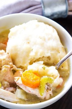 a white bowl filled with chicken and dumplings next to a napkin on a table