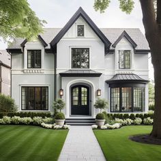 a large white house with black trim and windows on the front door is surrounded by lush green grass