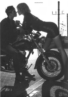 black and white photograph of a man kissing a woman on a motorcycle in the street