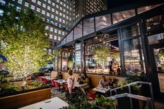 people sitting at tables in an outdoor restaurant with trees and lights on the outside wall