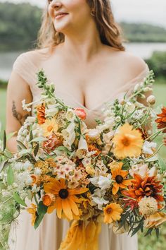 a woman holding a bouquet of sunflowers and other flowers in her hands while standing on the grass