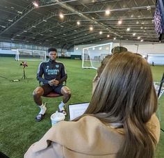 a man sitting on top of a chair in front of a laptop computer next to a soccer field