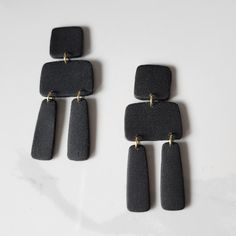 three rectangular black stone earrings on a white surface with gold ear wires hanging from them