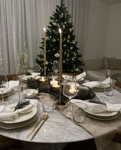 a table set for christmas dinner with candles, plates and napkins in front of a decorated christmas tree