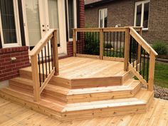 a wooden deck with steps and railings in front of a brick house