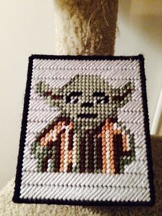 a close up of a stuffed animal near a cross stitch pattern on a wall hanging