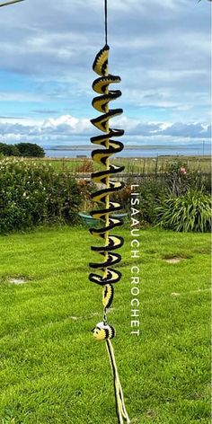 a wind chime in the shape of a spiral on top of green grass with blue sky and clouds behind it