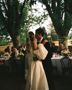 a bride and groom kissing in front of an outdoor dining table at their wedding reception