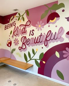 a bench sitting in front of a wall with flowers painted on it and the words being kind is beautiful