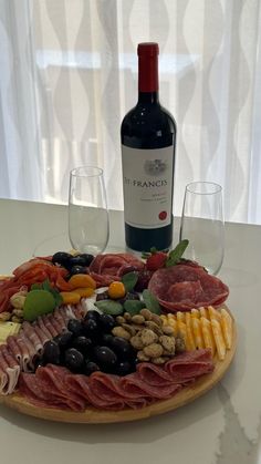 a wine bottle and two glasses on a table next to a platter with meats