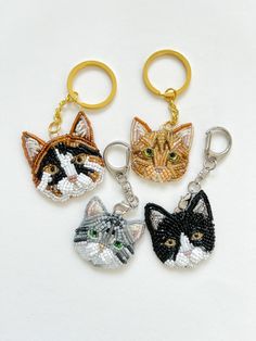 four keychains with cats on them sitting next to each other in different colors