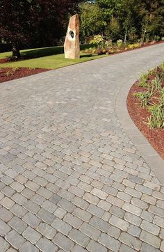 a brick walkway with a rock in the middle and grass around it on both sides