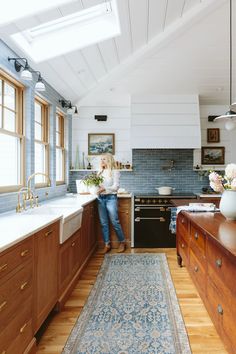 a woman standing in a kitchen next to a stove top oven under a skylight