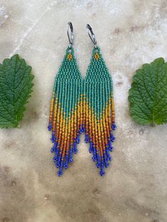 two pairs of beaded earrings sitting on top of a table next to green leaves