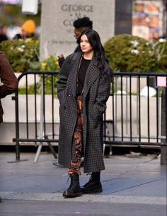 a woman is standing on the sidewalk in front of a fence and looking at something