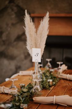 the table is set with wine glasses, candles and pamond feathers for centerpieces