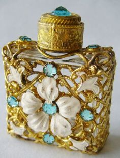 an ornate gold and white perfume bottle with blue stones