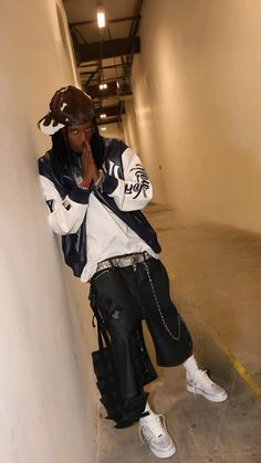 a young man leaning against a wall with his hand on his face and wearing white sneakers