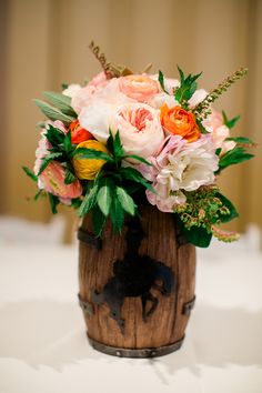 a wooden vase filled with lots of flowers on top of a white cloth covered table