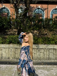 a woman with long blonde hair standing in front of a brick building wearing a plaid dress