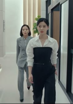 two women in business attire walking down a hallway with one woman looking at the camera