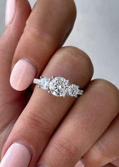 a woman's hand with pink manicured nails holding a three stone engagement ring