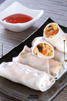 three spring rolls on a black plate with dipping sauce in a bowl next to it