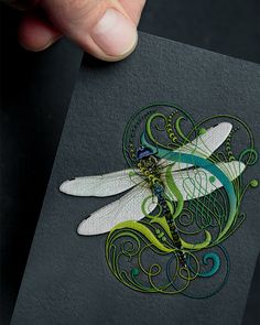 a hand holding up a card with a dragonfly on it's front and side