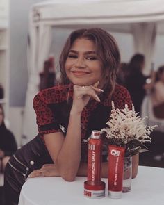 a woman sitting at a table with two cans of sodas and flowers in front of her