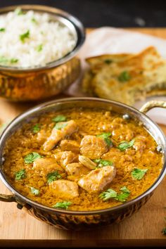 two bowls filled with curry and rice on top of a wooden table next to bread