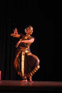 a woman is dancing on stage with her hands in the air while wearing a black and gold dress