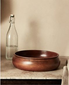 a wooden bowl sitting on top of a counter next to a glass bottle and towel