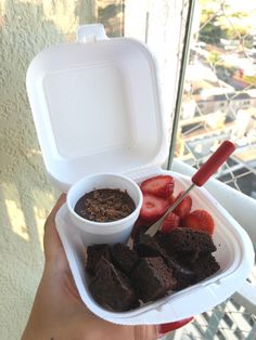 a person holding up a white container with brownies, strawberries and ice cream