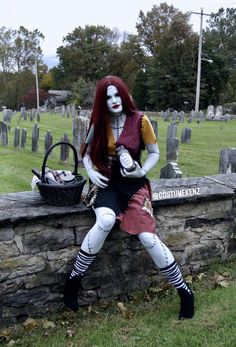 a woman dressed as a skeleton sitting on top of a stone wall next to a cemetery