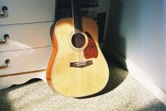 an acoustic guitar sitting on the floor next to a dresser