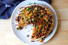 a white plate topped with a pizza covered in cheese and toppings on top of a wooden table