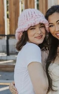 two women in white shirts and pink hats posing for the camera with their arms around each other