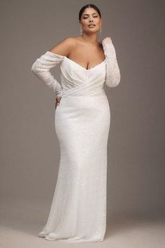 a woman in a white gown with long sleeves and an off the shoulder top is posing for