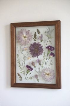 a wooden frame with pressed flowers in it on the wall next to a white wall