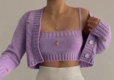 a woman wearing a purple sweater and white skirt is posing with her hands on her hips