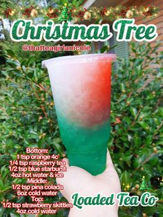 a hand holding up a green and red drink in front of some bushes with christmas lights