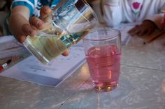 a person pouring liquid into a glass on top of a table