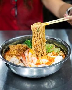 a person holding chopsticks above a bowl of food with noodles and vegetables on it