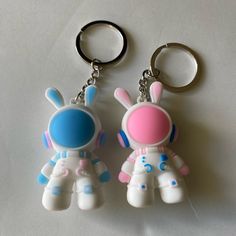 two plastic key chains are sitting next to each other on a white surface, one is pink and the other is blue