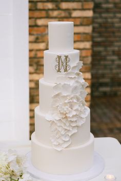 a three tiered white wedding cake with flowers on the top and monogrammed initials