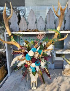 a vase with flowers and antlers on a wooden table in front of a fence