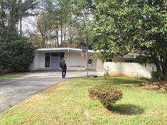 a man walking towards a house in the middle of a driveway with trees around it